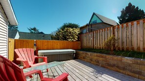 A backyard patio with a glass table, red chairs, a hot tub, and a wooden fence.