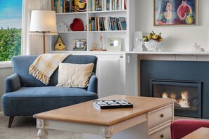 A living room with a blue armchair, a wooden coffee table, a fireplace, and a bookshelf filled with books.