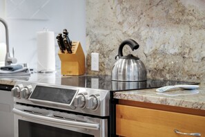 Une cuisine équipée d’une cuisinière en acier inoxydable, d’une bouilloire et d’un plan de travail en marbre.
