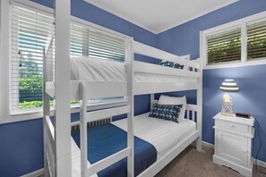 Een slaapkamer met een stapelbed, raam, nachtkastje en lamp.