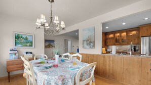 A dining area with a table set for four, surrounded by wooden chairs. A chandelier hangs from the ceiling, and there are paintings on the walls. - OCEAN FRONT: SEAS THE DAY:  Seaside Vacation Homes, Inc Managed  (Seaside)
