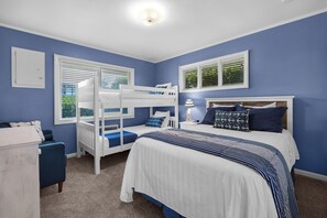 Une chambre avec un lit superposé, un lit simple, une table de chevet et une commode.