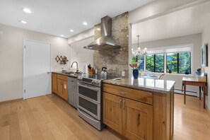 Een moderne keuken met een centraal eiland, roestvrijstalen apparatuur, houten kastjes en een groot raam met uitzicht op groen.