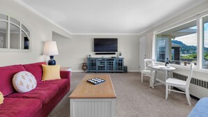 A modern living room with a red sofa, a wooden coffee table, a flat-screen TV, and a dining area with a white table and chairs. - OCEAN FRONT: SEAS THE DAY:  Seaside Vacation Homes, Inc Managed  (Seaside)