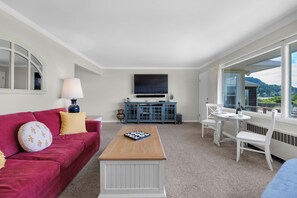 Een moderne woonkamer met een rode bank, een houten salontafel, een flatscreen televisie, en een eethoek met een witte tafel en stoelen.