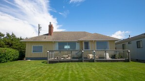 A single-story house with a covered patio area, large windows, and a chimney. - OCEAN FRONT: SEAS THE DAY:  Seaside Vacation Homes, Inc Managed  (Seaside)