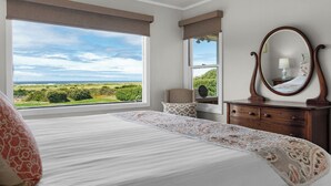 A bedroom with a large window, a bed with patterned bedding, a dresser, and a mirror. - OCEAN FRONT: SEAS THE DAY:  Seaside Vacation Homes, Inc Managed  (Seaside)
