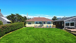 A residential property with a well-maintained lawn, a covered patio with seating, and a neighboring house. - OCEAN FRONT: SEAS THE DAY:  Seaside Vacation Homes, Inc Managed  (Seaside)