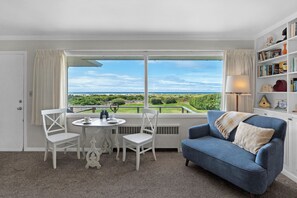 Een kamer met balkon, een eettafel met stoelen, een blauwe bank en een boekenkast.