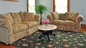 Een woonkamer met twee gestreepte banken, een ronde salontafel en een groot raam met gordijnen.