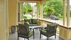 Een overdekt terras met een tafel en stoelen, zuilen en uitzicht op de straat.