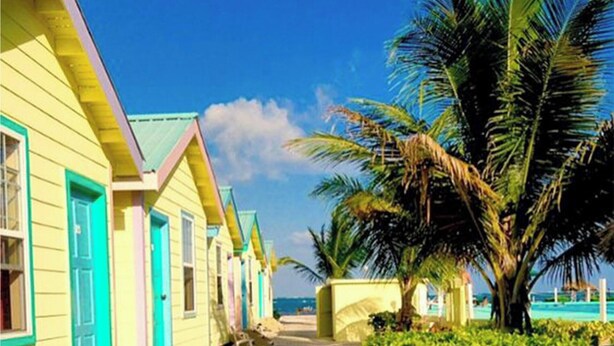 A row of colorful beach cottages with a clear view of the ocean. - Cabana with a pool and garden view (San Pedro)