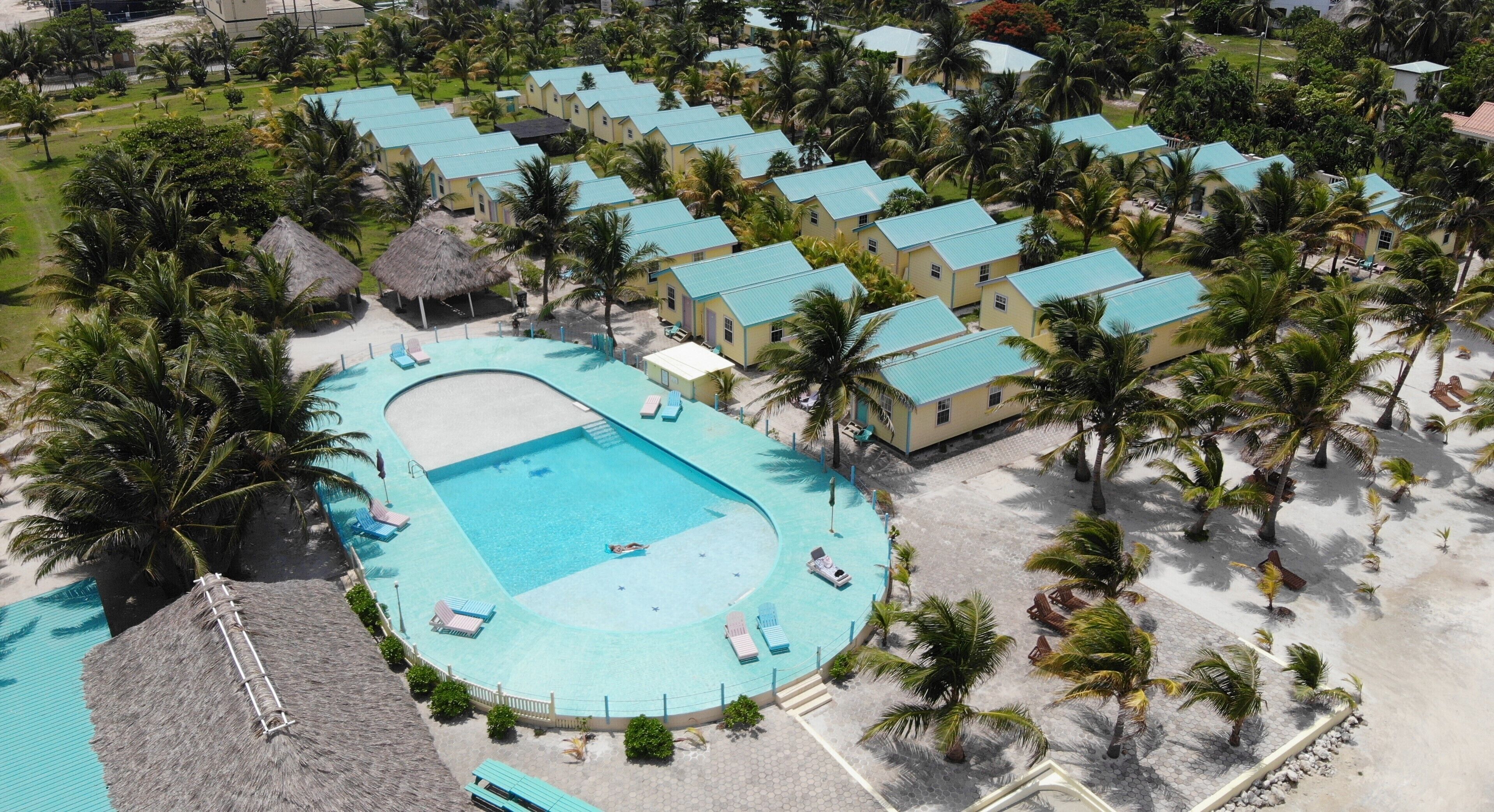 Luchtbeeld van een resort met een centraal zwembad, meerdere gastvillas en omliggende palmbomen.