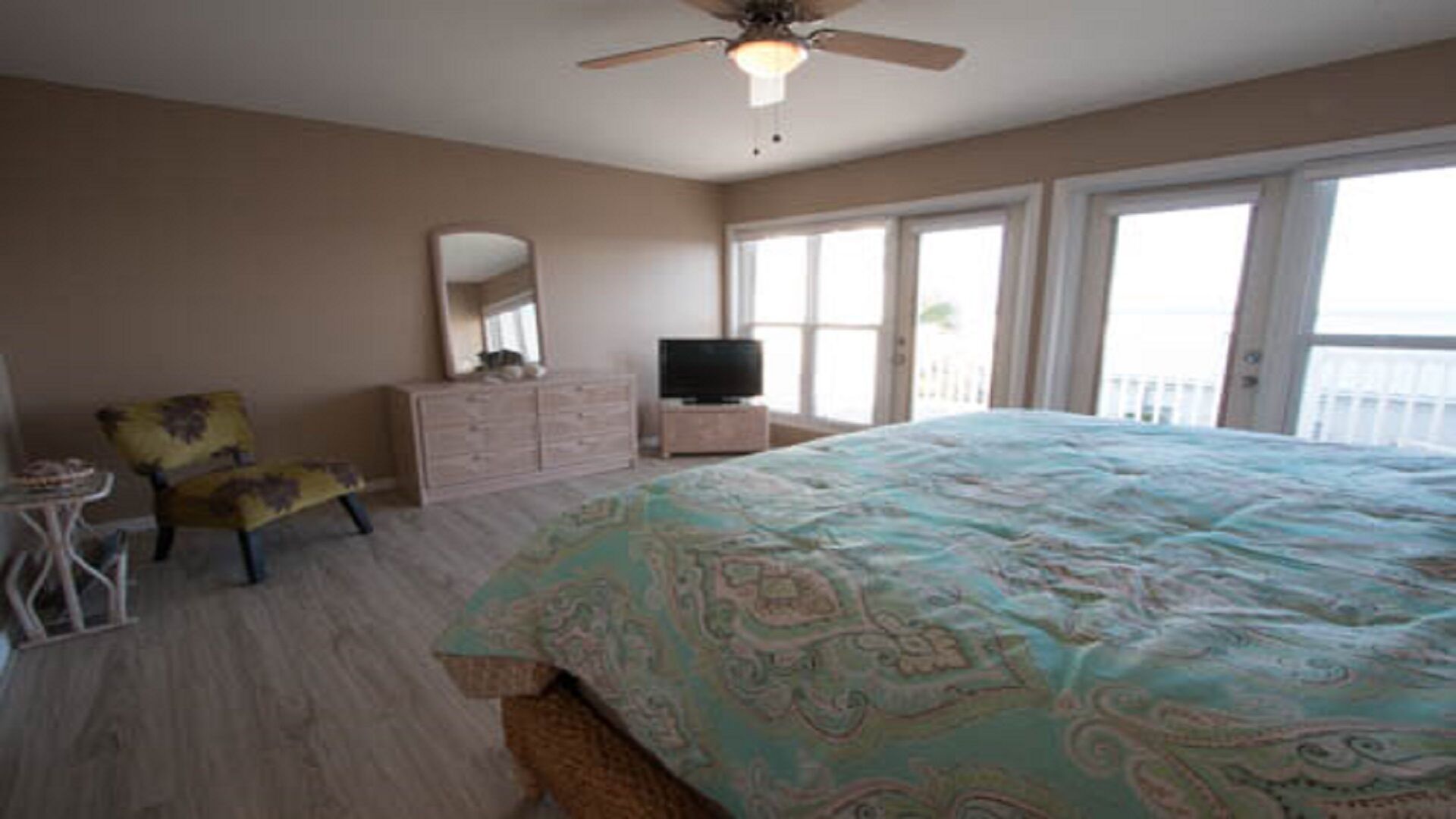A bedroom with a bed, a dresser, a chair, a television, and a balcony with a view.