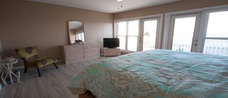 A bedroom with a bed, a dresser, a chair, a television, and a balcony with a view.