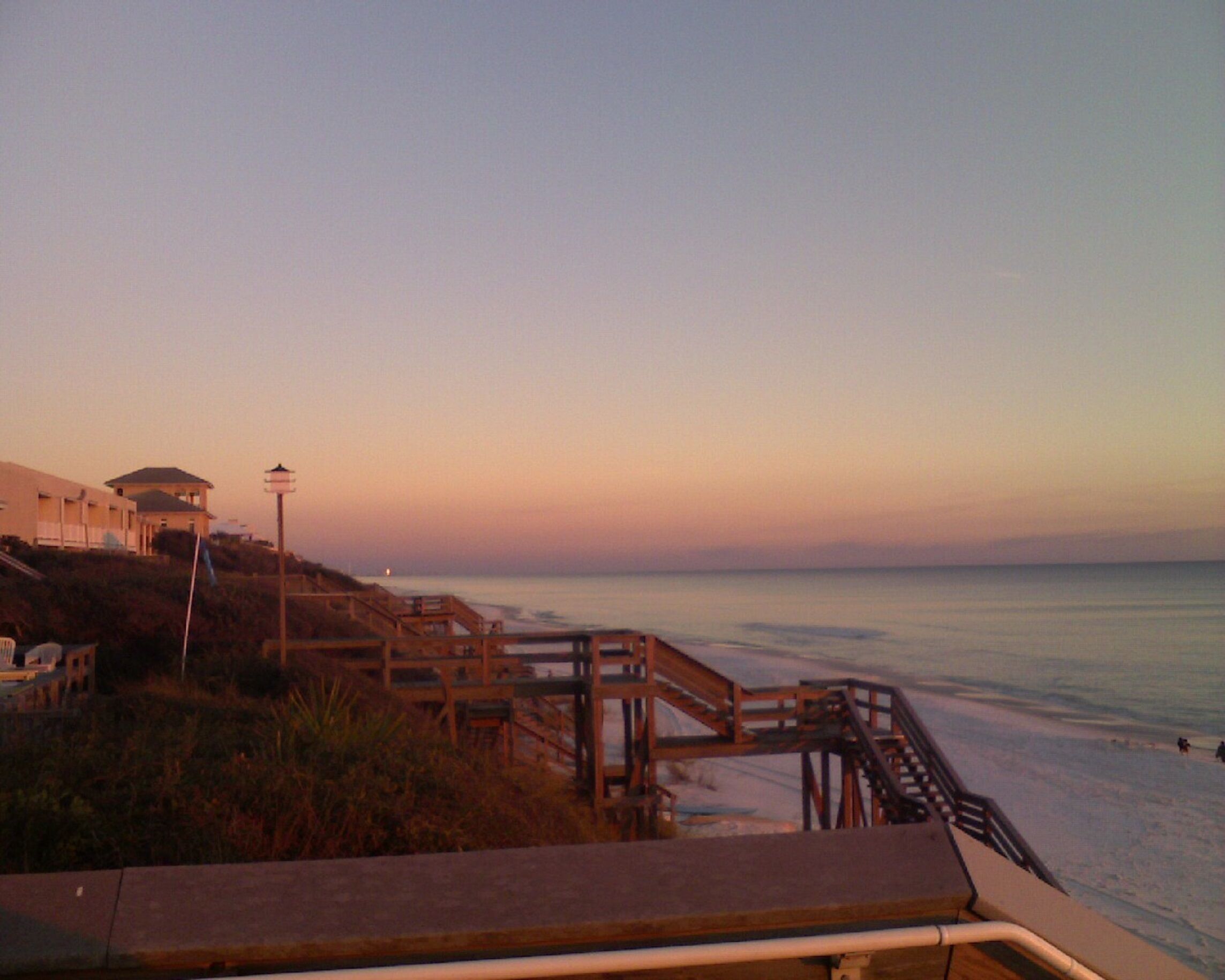 A beach with a wooden walkway leading to a building with a covered area.