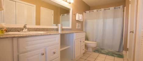 A bathroom with a sink, mirror, toilet, and shower curtain.