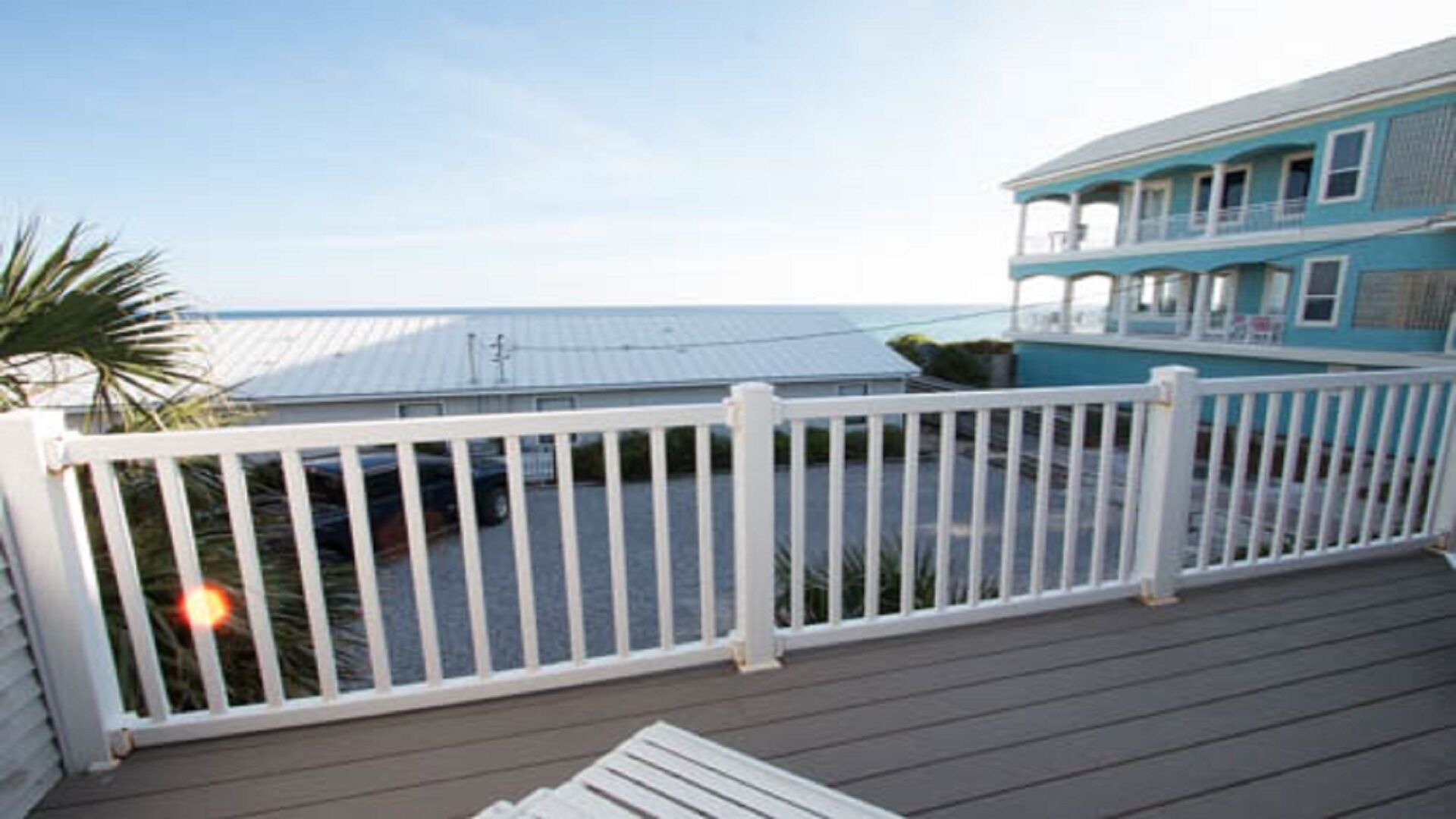 A wooden deck with a white railing, overlooking a body of water and a building with a blue facade.