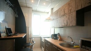 Una cocina compacta con estufa a gas, un lavamanos y un microondas. Hay una pequeña zona de bar con taburetes y una computadora portátil sobre la encimera.