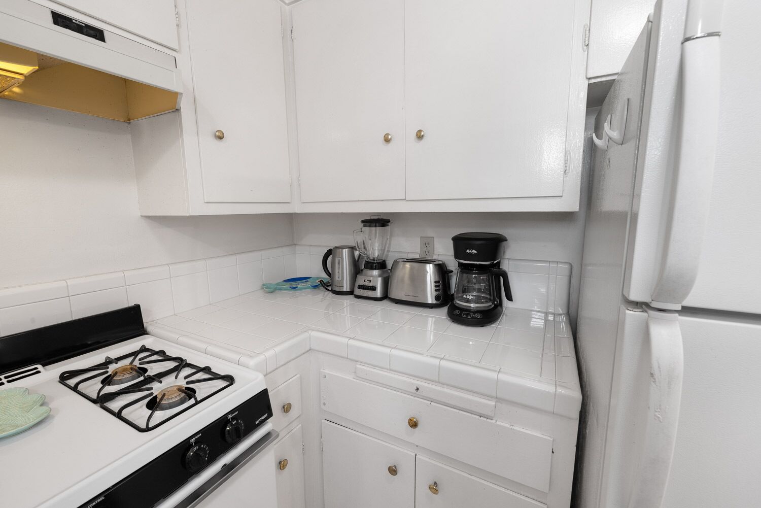 Une cuisine avec des meubles blancs, une cuisinière à gaz, une machine à café et un grille-pain.