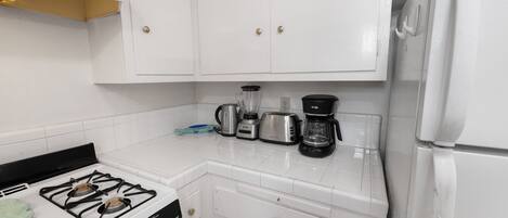 Une cuisine avec des meubles blancs, une cuisinière à gaz, une machine à café et un grille-pain.