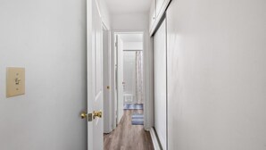 A narrow hallway with white walls and a wooden floor leading to a room with a blue carpet. - Cozy Condo With New AC, Steps from Balboa Ferry and Peninsula Beach Access (Balboa Island, Newport Beach)