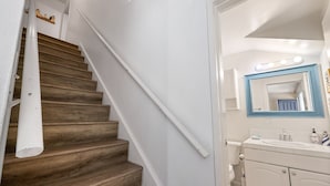 A staircase with wooden steps and white walls, leading to a bathroom with a white sink, mirror, and cabinet. - Cozy Condo With New AC, Steps from Balboa Ferry and Peninsula Beach Access (Balboa Island, Newport Beach)