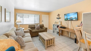 A living room with a sofa, coffee table, TV, and a bookshelf. - Cozy Condo With New AC, Steps from Balboa Ferry and Peninsula Beach Access (Balboa Island, Newport Beach)