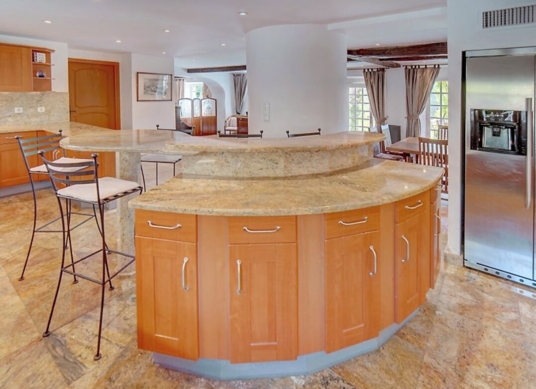 A spacious kitchen with a curved island, wooden cabinets, and a stainless steel refrigerator.