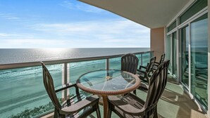 A balcony with a glass table and chairs, overlooking a body of water.