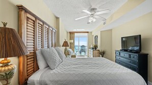 A bedroom with a bed, a ceiling fan, a TV, and a view to the outside.