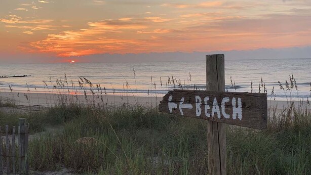Un panneau en bois sur lequel est écrit le mot « PLAGE » et qui indique la direction de l’océan.