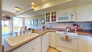 A modern kitchen with white cabinetry, a built-in microwave, a stove, and a sink. - OCEAN FRONT: DESTRESS RX: Seaside Vacation Homes, Inc Managed (Seaside)