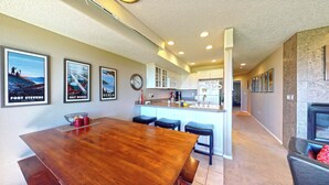 A modern kitchen with white cabinets, a wooden dining table, and a bar area. - OCEAN FRONT: DESTRESS RX: Seaside Vacation Homes, Inc Managed (Seaside)