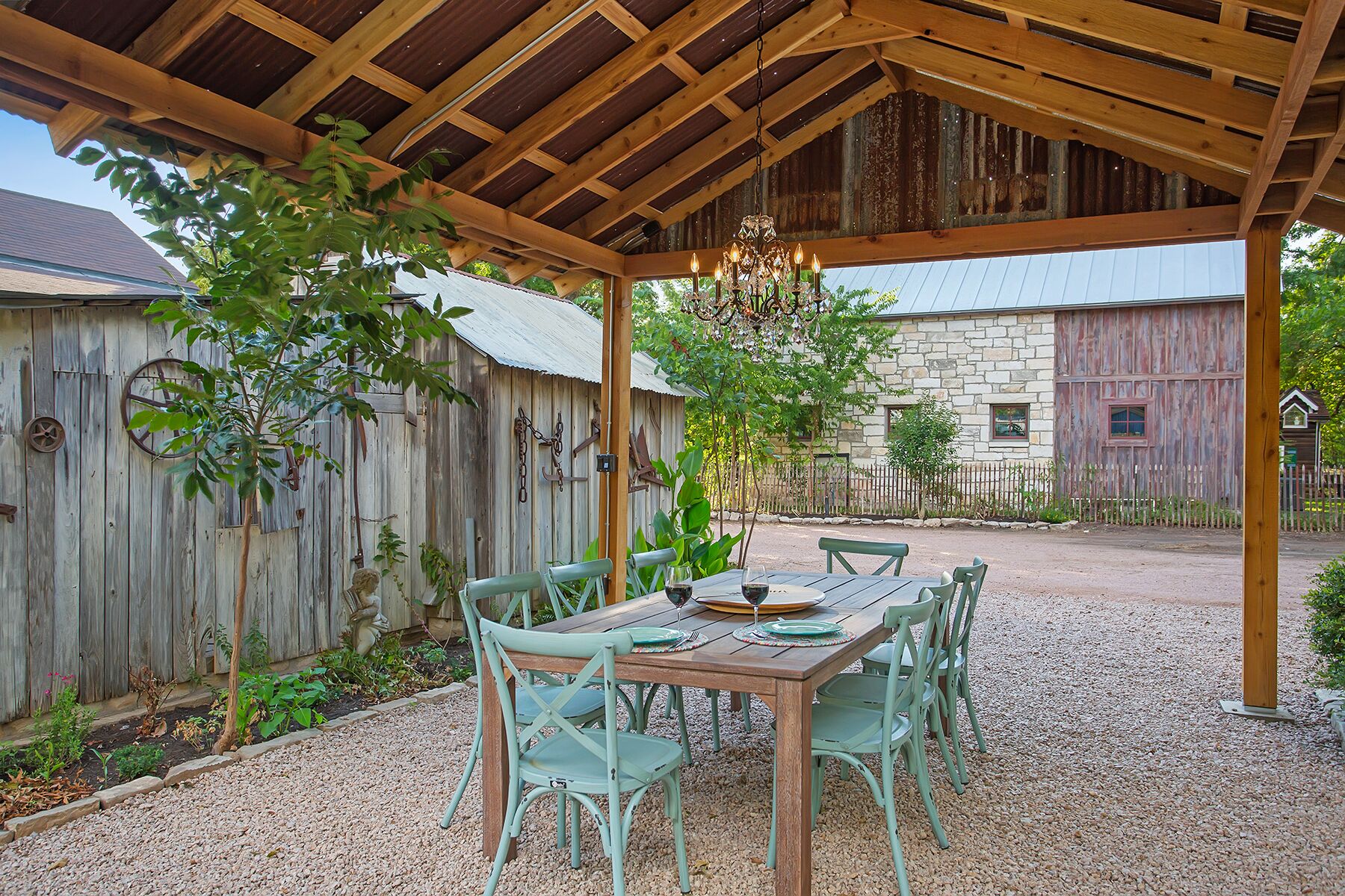 An outdoor patio with a wooden pergola, a table set for dining, and rustic stone buildings in the background.