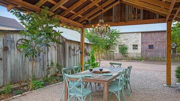 An outdoor patio with a wooden pergola, a table set for dining, and rustic stone buildings in the background.