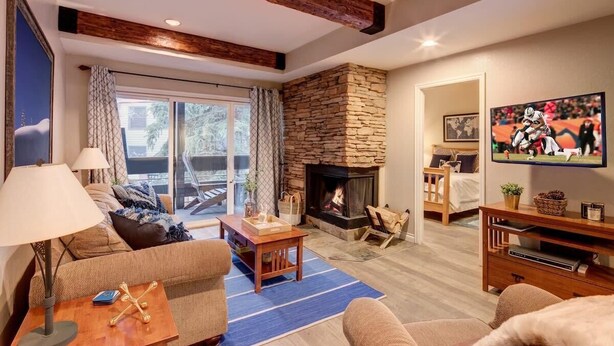 Una sala de estar acogedora con chimenea de piedra, un sofá, una mesa de centro y un televisor.