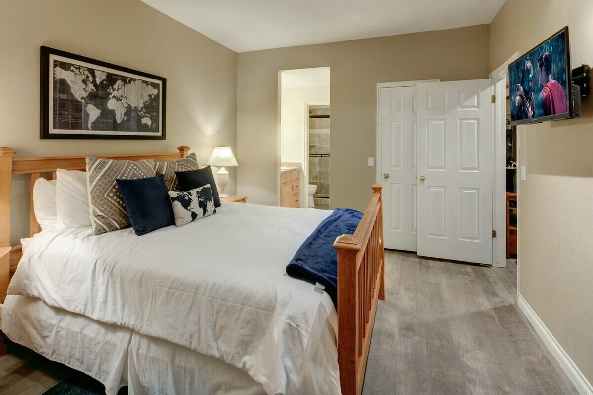 A bedroom with a bed, a world map on the wall, a TV, and a door leading to another room.