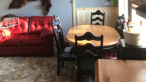 A dining area with a wooden table and chairs, a chandelier, a mounted animal hide, and a red sofa. - Cozy "tiny home" Cabin with amazing views (Mountain View)