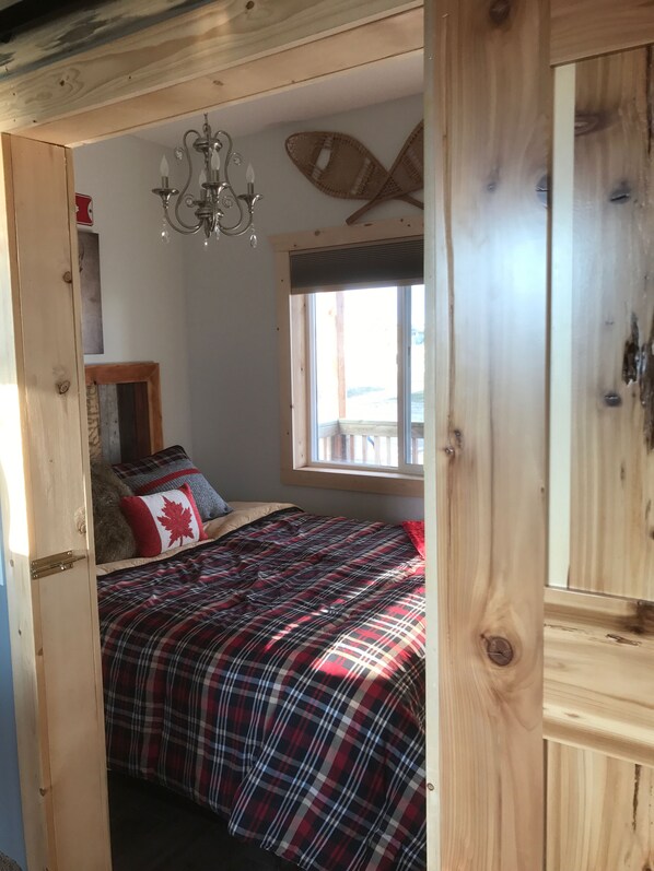 Une chambre confortable avec une couvre-lit à carreaux, un plafond en bois, une fenêtre donnant sur un beau paysage et un lustre.