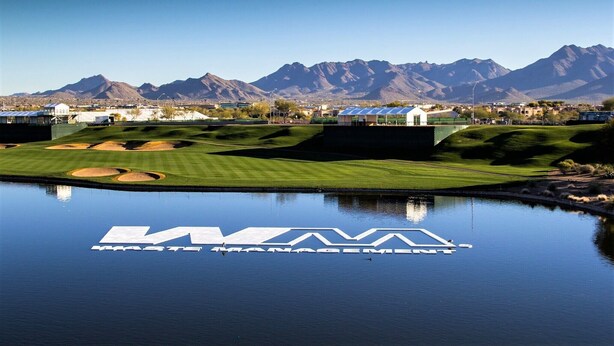 Un campo de golf con un cuerpo de agua que refleja el texto "WASTE MANAGEMENT" y montañas al fondo.