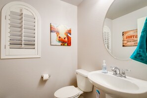 Une salle de bain avec des toilettes, un lavabo et une fenêtre équipée de stores.