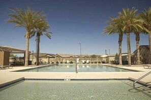 Une piscine bordée de palmiers, avec des chaises longues et un ciel dégagé.