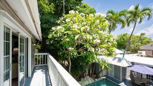Un espace aménagé au bord de la piscine, avec une balustrade blanche, une petite piscine et une végétation luxuriante comprenant des arbres en fleurs et des palmiers.