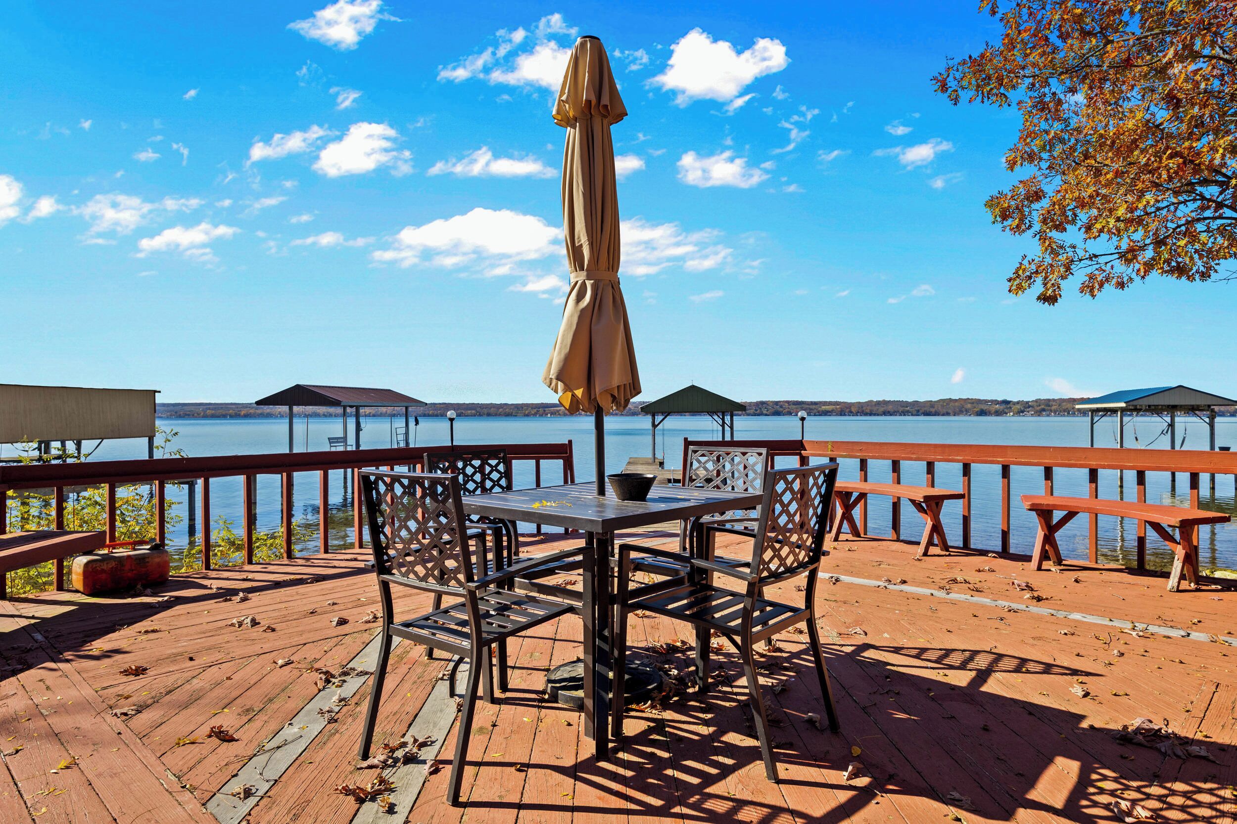 A wooden deck with a table and chairs, an umbrella, and a view of a lake.