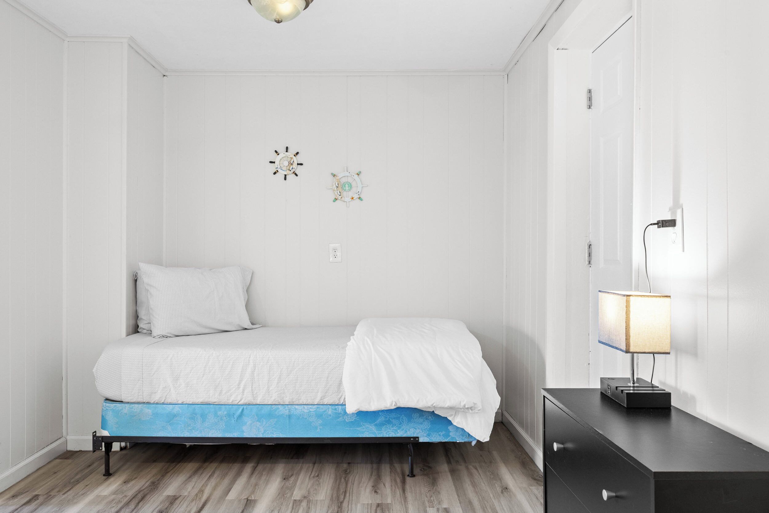 Een kleine, verzorgde slaapkamer met een enkel bed, een nachtkastje met een lamp en een dressingkast.