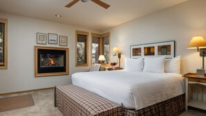 A bedroom with a large bed, a fireplace, a ceiling fan, and a nightstand with a lamp. - Tamarack - Steps to the Slopes + ASE Transportation (Snowmass Village)