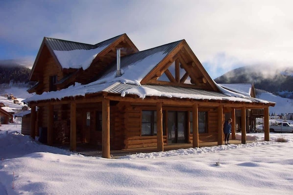 A wooden cabin with a sloped roof, large windows, and a chimney.