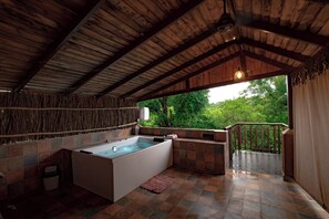 A wooden-roofed bathroom with a large bathtub, tiled walls, and a view of greenery outside.