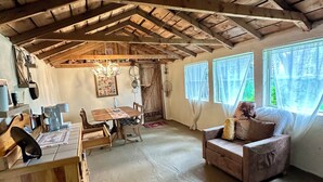 A rustic interior with a wooden ceiling, a dining table, a sofa, and a window with curtains.